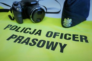Kamizelka odblaskowa z napisem Policja Oficer Prasowy, aparat i czapka policyjna